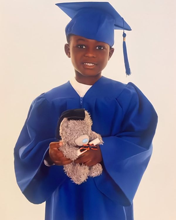 Young child in a blue graduation cap and gown holding a teddy bear and a rolled certificate